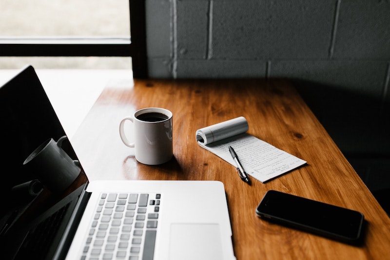 A laptop, phone, notepad, and cup of coffee on a desk -- some of the tools to aid in inventorying your furniture